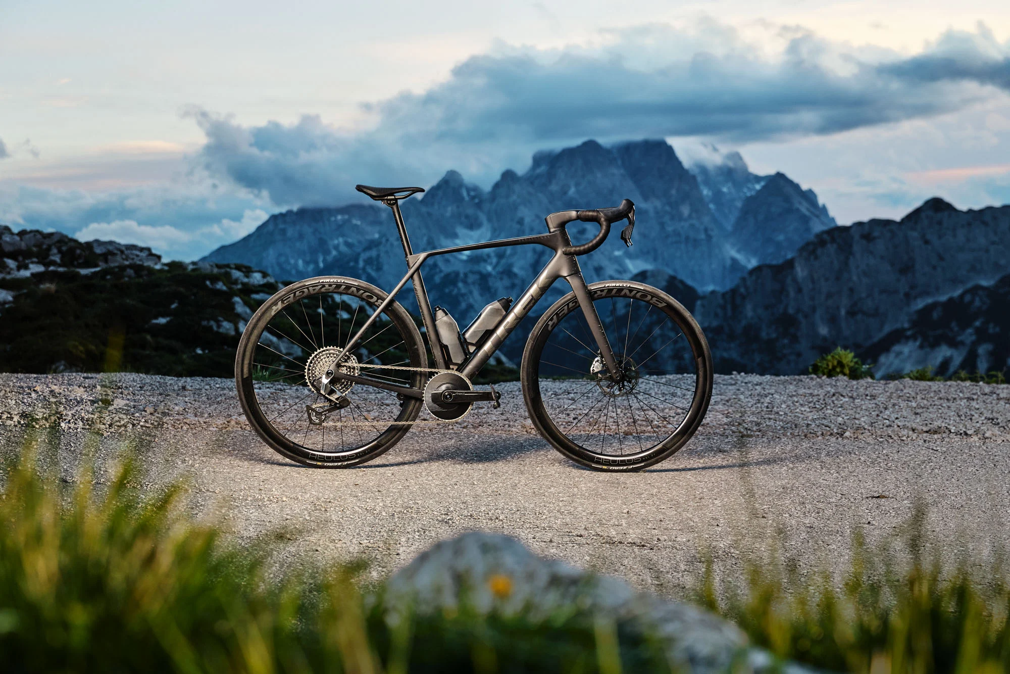 Trek Domane 5ª geração parada em uma estrada de cascalho, com as montanhas ao entardecer ao fundo